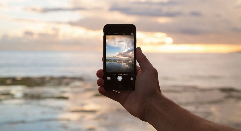Uma pessoa tira uma foto com celular de um horizonte na praia.