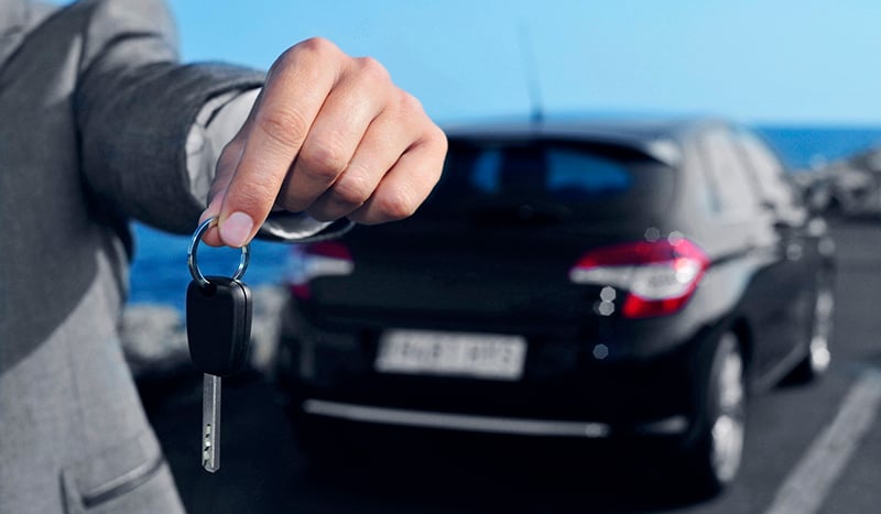 Pessoa segura as chaves de um carro em frente ao veículo, que está desfocado