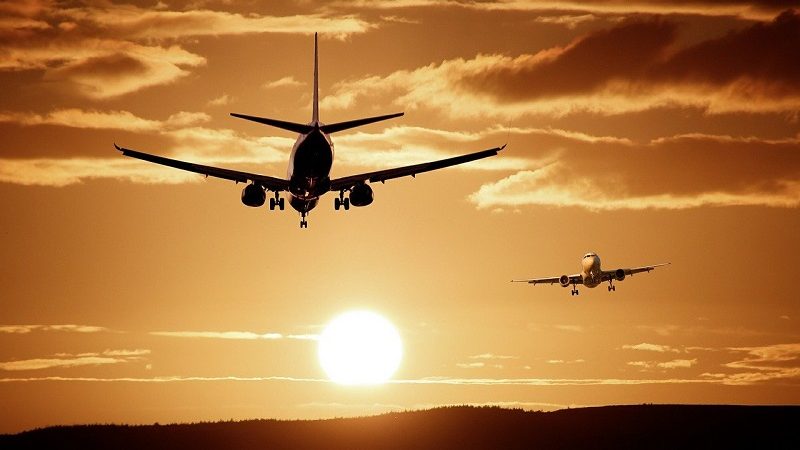 Dois aviões voando em direções opostas no céu em pleno pôr-do-sol. O da frente está em direção ao sol e o segundo de frente para quem vê a fotografia.