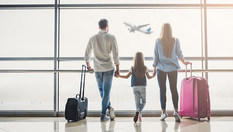 Família olha avião decolando da janela do aeroporto