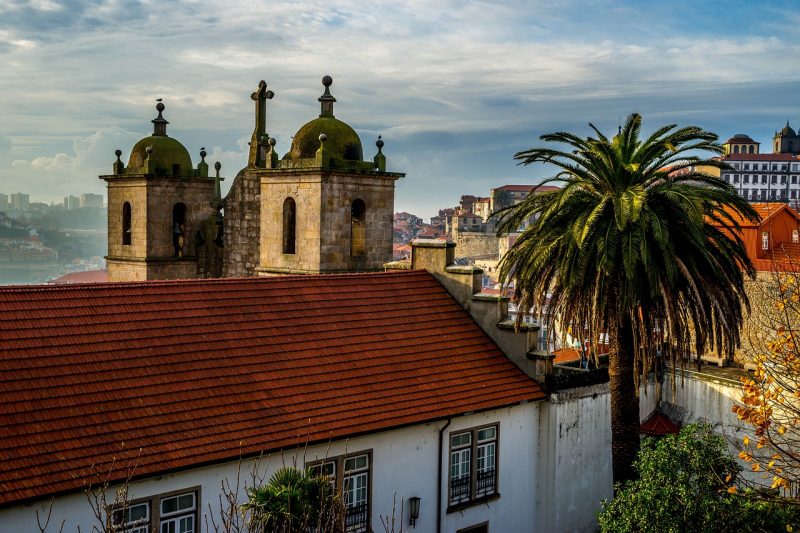 Vista de cima de uma cara em Porto, com uma igreja à frente e uma palmeira ao lado.