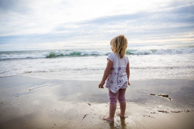Criança na praia diante do mar