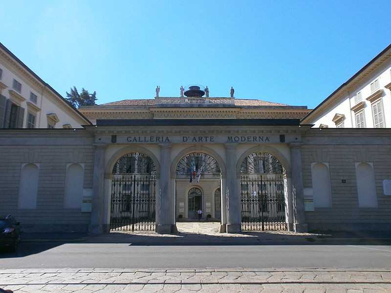 Fachada da Galeria de Arte Moderna em Milão. Nota-se arcos nos portões do museu e o nome do museu inscrito acima dos portões