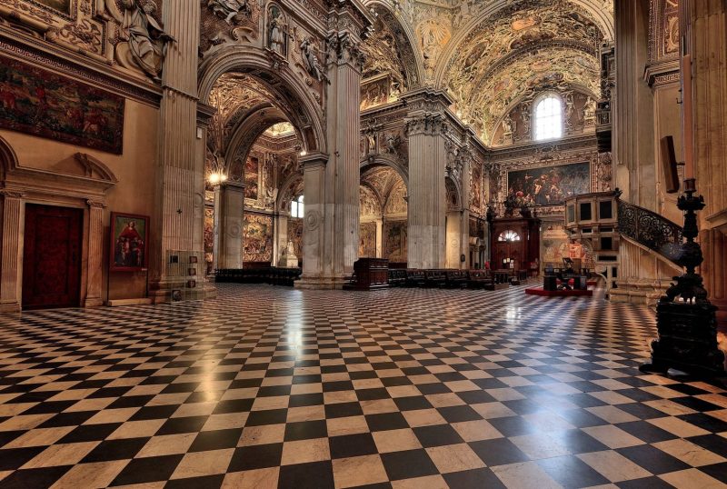 Interior da Santa Maria Maggiore na Itália. Nota-se um piso quadriculado preto e branco e uma estrutura de arcos antiga.