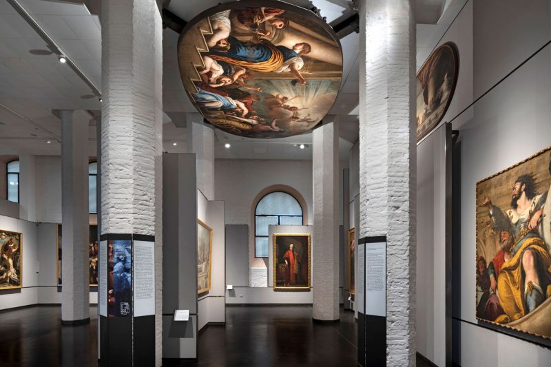Interior da Galeria da Academia em Veneza. O lugar expõe diversos quadros, sendo um deles pendurado no teto.