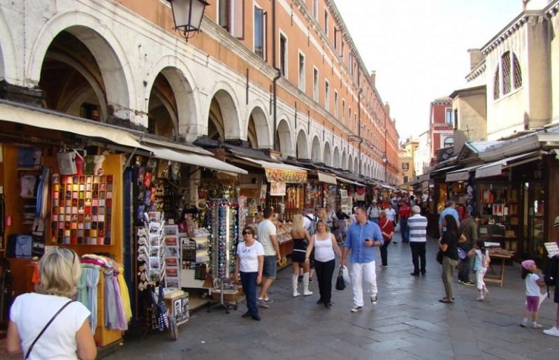Pessoas andam por rua com diversas lojinhas de souvenirs em Veneza.