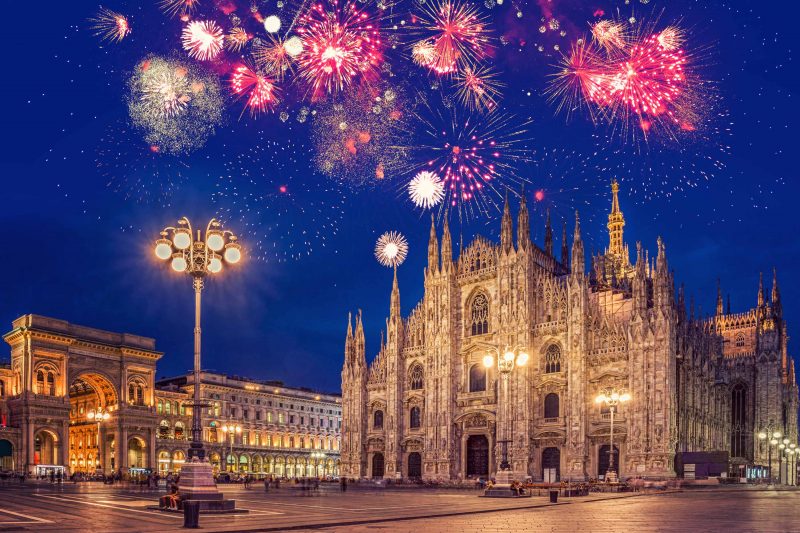 Piazza del Duomo no réveillon em Milão. Nota-se fogos de artifício coloridos (em sua maioria tons de rosa) estourando em cima da Catedral de Milão