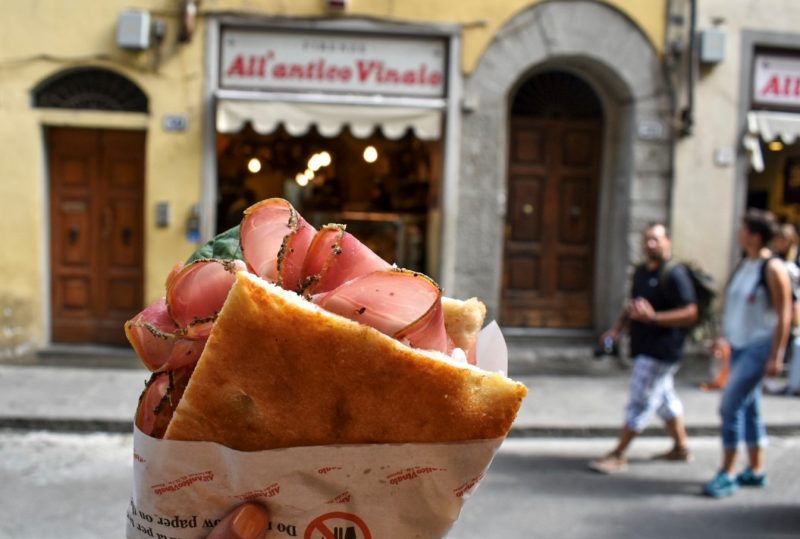 Pessoa segura sanduíche com carne em frente ao All'Antico Vinaio em Milão