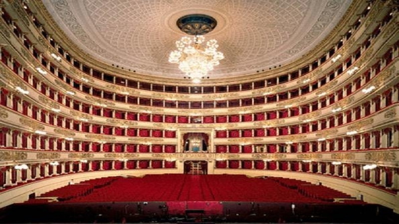 Interior de sala no Teatro Escala em Milão. Nota-se que todos os móveis são vermelhos e há detalhes dourados por todo lugar, além de um lustre no meio do teto.