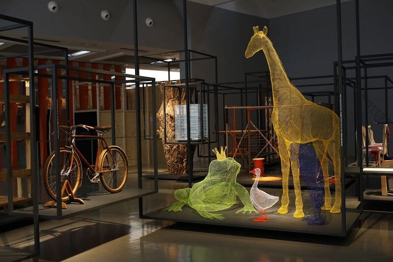 Interior do Museu La Triennale em Milão. Entre as peças expostas, nota-se uma bicicleta em uma parte da exposição e animais gigantes em outra.