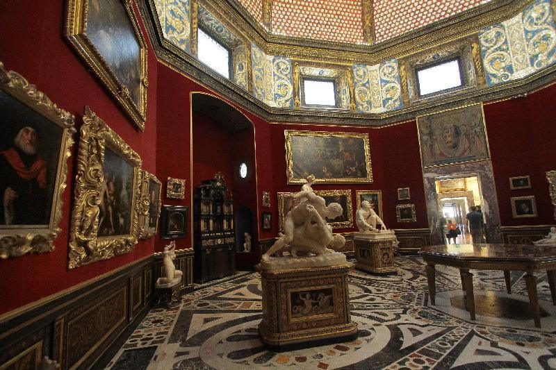 Sala no interior da Museu Galleria degli Uffizi em Florença. Nota-se quadros e escultura em exposição e as paredes da sala são vermelhas.