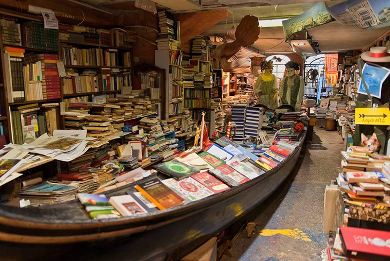 Interior da Libreria Acqua Alta em Veneza. Nota-se um barco com muitos livros dentro do lugar.