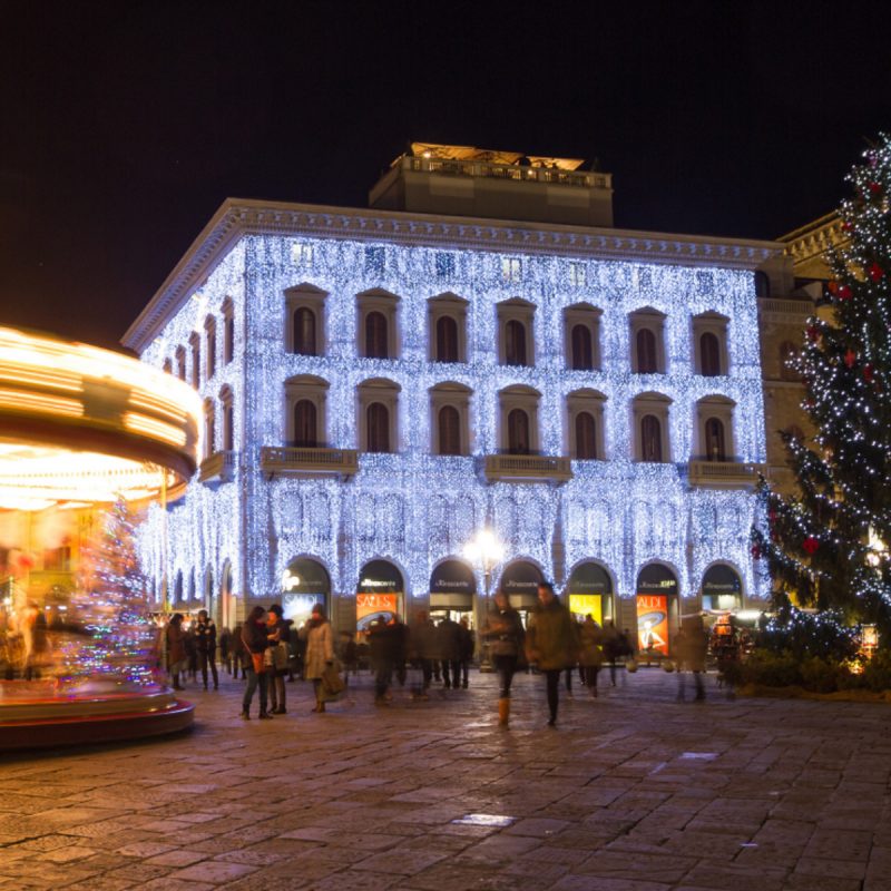 Prédio em Florença coberto de pisca-piscas no Natal. Nota-se um carrossel à esquerda e uma árvore de natal à direita.