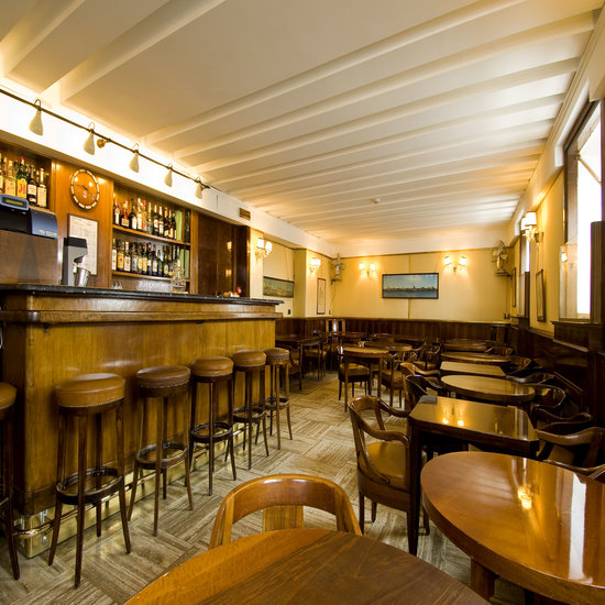 Interior do Harry's Bar em Veneza. O lugar, tem móveis predominantemente amadeirados e a decoração transita em tons amarelados e marrons.