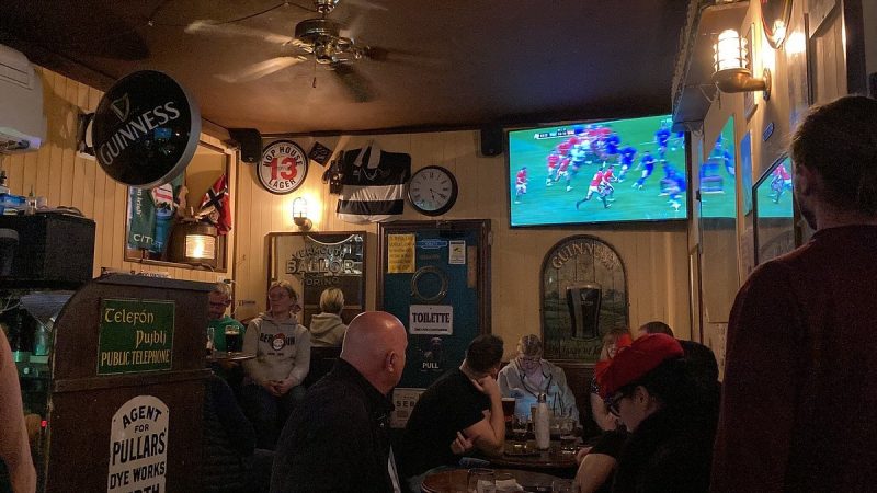 Interior do The Irish Pub em Veneza. Nota-se várias pessoas no pub, sendo que algumas assitem a um jogo de futebol na televisão.